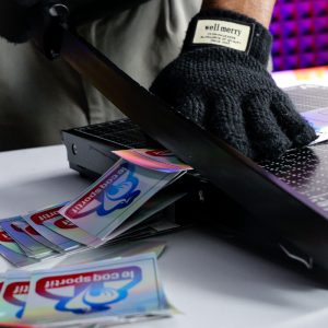 Découpe manuelle de stickers holographiques Le Coq Sportif dans l’atelier de production.