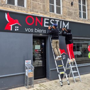 Installation de l’enseigne Onestim par les techniciens Persecom sur la façade du commerce.