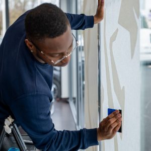 Technicien Persecom posant la vitrophanie du lion Peugeot sur la vitrine intérieure du garage.