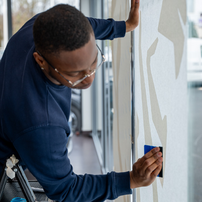 Technicien Persecom posant la vitrophanie du lion Peugeot sur la vitrine intérieure du garage.
