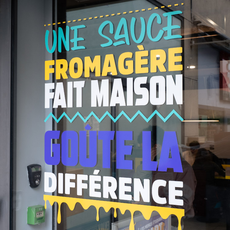 Lettrage adhésif coloré appliqué sur une vitrine dans le cadre d’un flocage de vitrine.