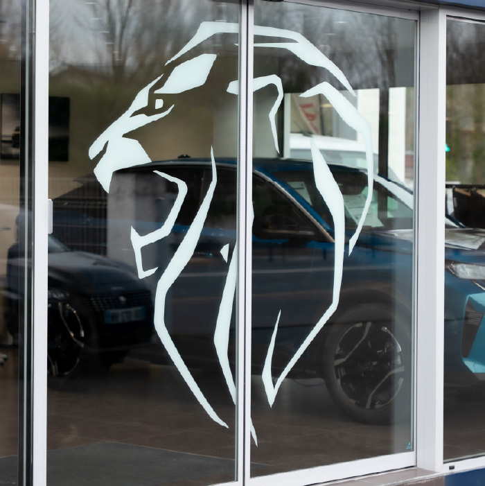 Gros plan du logo Peugeot en vitrophanie posé en intérieur sur la façade du garage Saône.