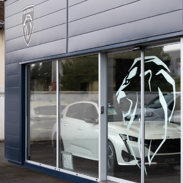 Vitrophanie grand format du logo Peugeot installée sur la vitrine du garage Saône à Lyon.