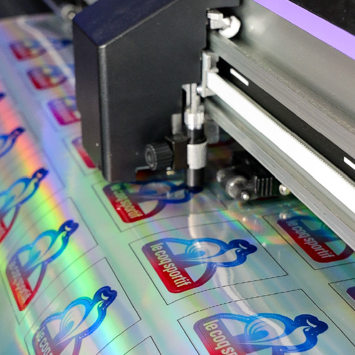 Machine de découpe en action sur des stickers holographiques Le Coq Sportif.