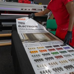 Technicien Persecom manipulant un adhésif publicitaire grand format IRSAP dans l’atelier.