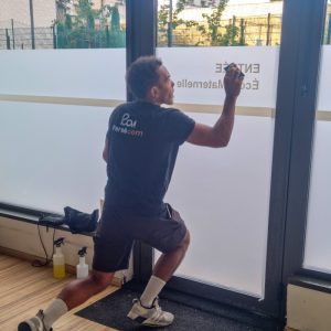 Installateur Persecom posant un film dépoli imprimé sur les vitres de l’école Les Lettres Dorées.