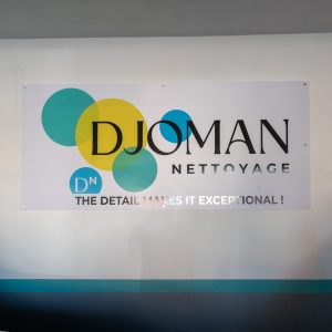 Grande plaque murale Djoman Nettoyage avec slogan imprimé et posée dans le garage.