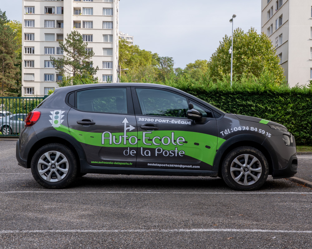 Voiture d’auto-école équipée d’un flocage publicitaire vert et noir sur les portières.